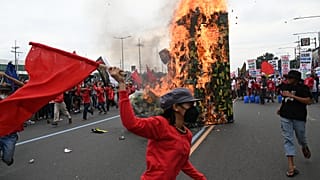 Protesters run past a giant military boot after setting it up on fire as they march towards Congress for a demonstration in Quezon City, suburban Manila on July 24, 2023