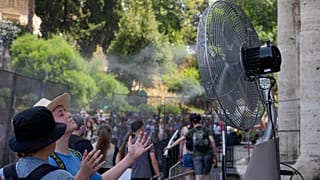 Touristen kühlen sich in der Nähe eines Ventilators ab, während sie in der Schlange vor dem Kolosseum in Rom stehen, 18. Juli 2023.