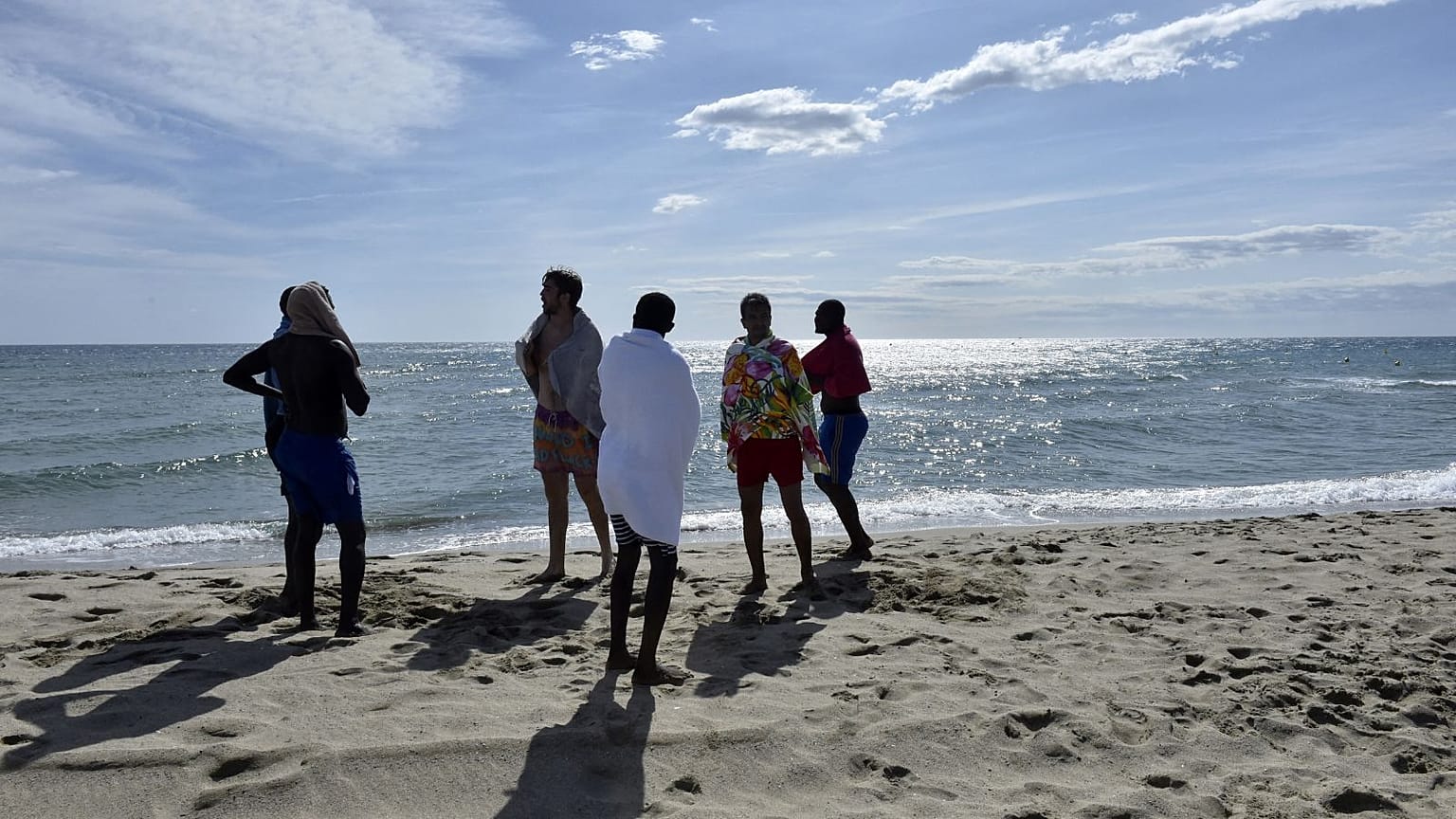Members of an association working to facilitate the social inclusion and professional integration of refugees and asylum seekers, and migrants stand on the beach