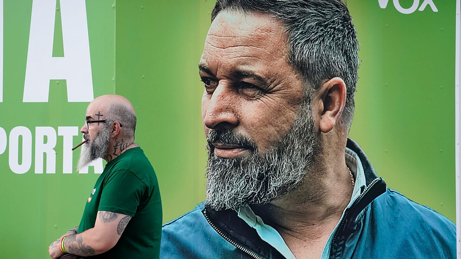 Um homem junto a um cartaz eleitoral do partido de extrema-direita Vox, que mostra o seu líder Santiago Abascal, à porta da sede do partido em Madrid.