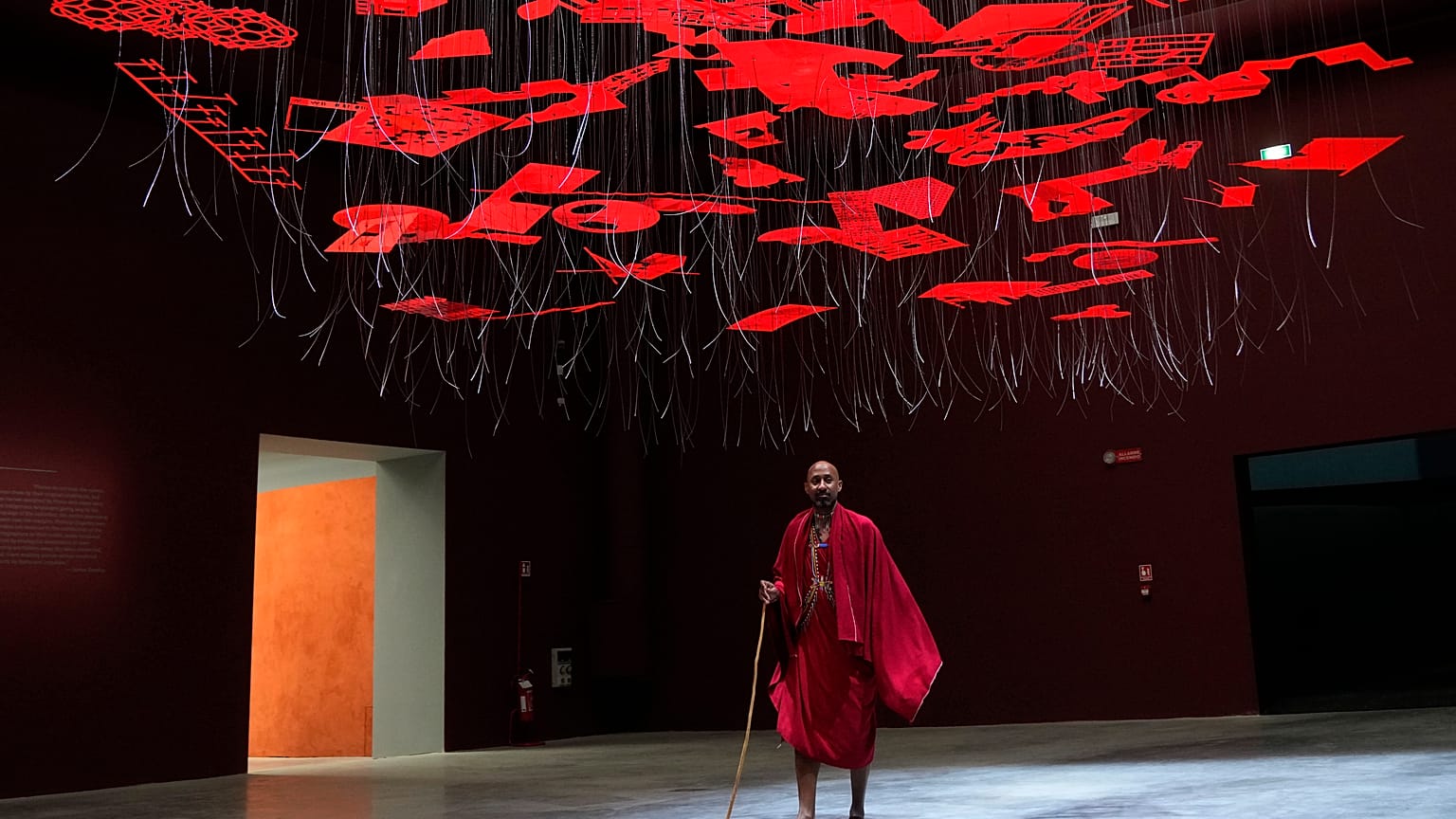 A man wearing traditional Masai clothes walks under an installation, at the Biennale International Architecture exhibition, in Venice, Italy, Wednesday, May 17, 2023. 