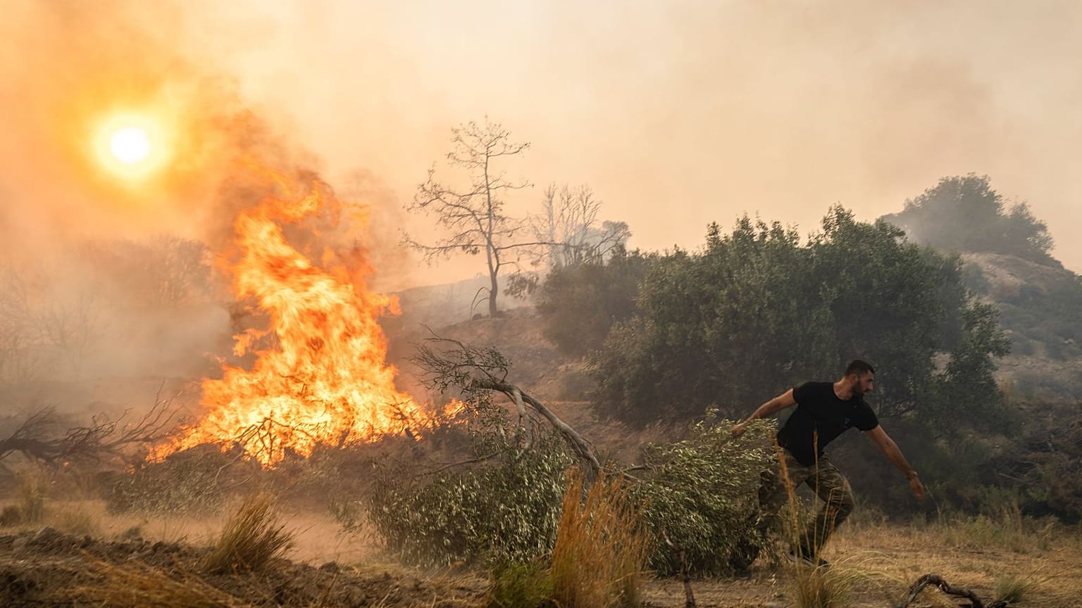 Ilias Kyriakou, 25, pulls an olive branch as a wildfire burns in Gennadi village, on the Aegean Sea island of Rhodes, southeastern Greece, 25 July 2023.