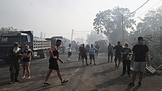 Residentes locales permanecen en la carretera durante un incendio forestal en la localidad de Nea Anchialos, cerca de la ciudad de Volos, Grecia central.