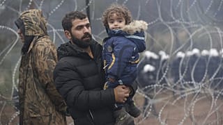 A migrant with a child walks along the barbed wire fence as other gather at the Belarus-Poland border near Grodno, Belarus, Nov. 14, 2021.