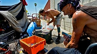 Two men pour ice into a bucket in "The Zone" homeless encampment in Phoenix, Arizona.
