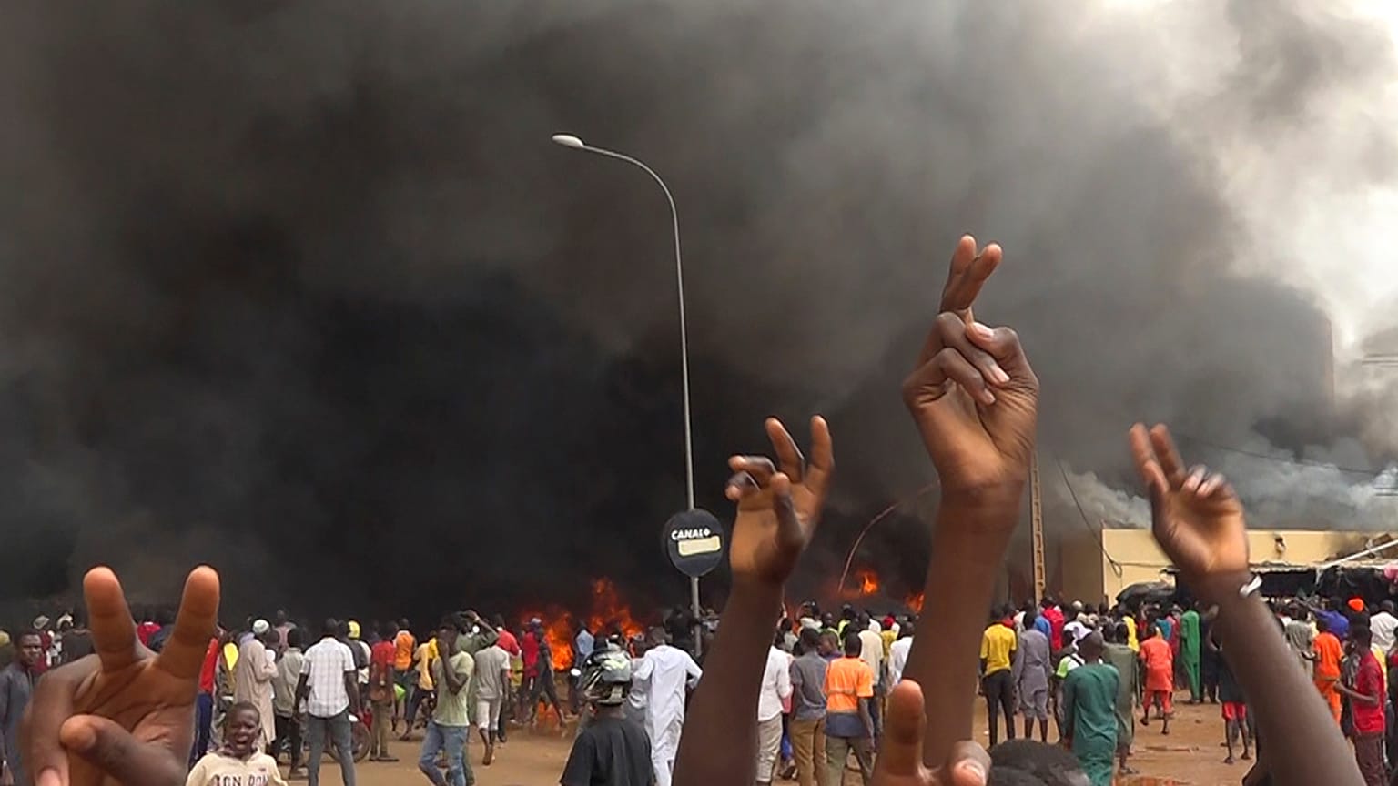 With the headquarters of the ruling party burning in the back, supporters of mutinous soldiers demonstrate in Niamey, Niger, Thursday, July 27 2023.