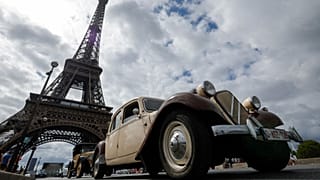 Car enthusiasts drive past the Eiffel tower during the 16th "Traversee estivale" vintage vehicles parade through Paris on July 30, 2023.