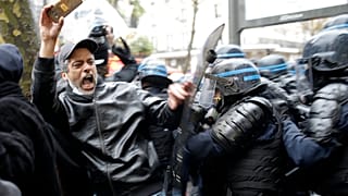 Riot police officers charge a man holding his phone during a protest rally in Paris, France