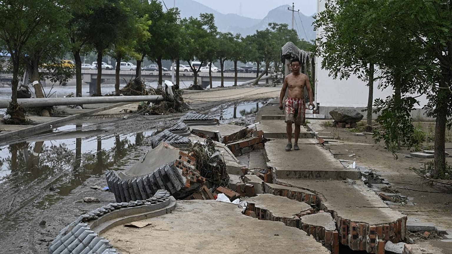 Un uomo cammina in bilico sui marciapiedi squarciati a Pechino, dopo l'alluvione