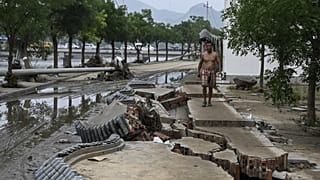 Un uomo cammina in bilico sui marciapiedi squarciati a Pechino, dopo l'alluvione
