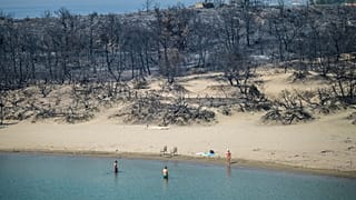Una mujer se adentra en el mar desde una playa en la que el fuego arrasó el bosque, en Glystra, cerca del pueblo de Gennadi, en el sur de la isla griega de Rodas.