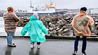 People stand in windy weather on the outer pier at Hirtshals Harbour, Denmark, Monday, Aug. 7, 2023.
