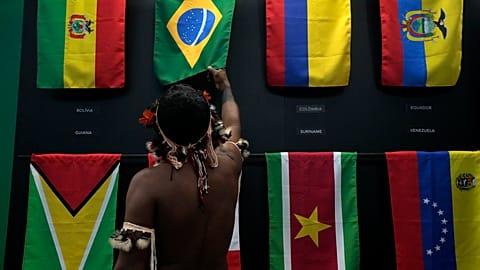 An indigenous man passes in a flag pavilion of the States parties to the Amazon Cooperation Treaty, during the Amazon Dialogue meetings in Belem, Brazil, Sunday, Aug. 6, 2023.