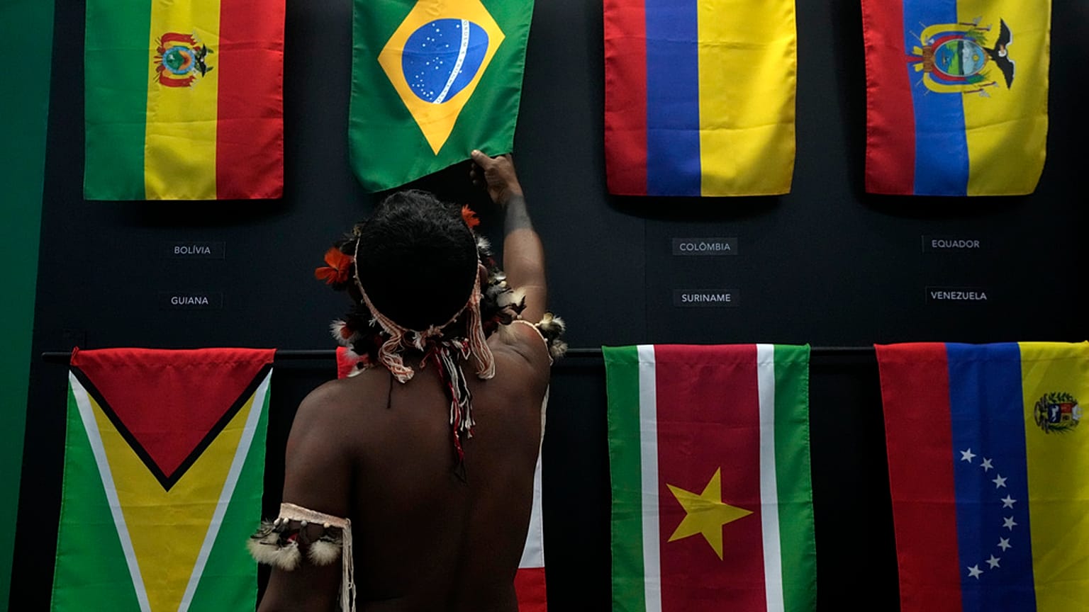 An indigenous man passes his hand over the Brazilian flag in a flag pavilion of the States parties to the Amazon Cooperation Treaty, during the Amazon Dialogue meetings.