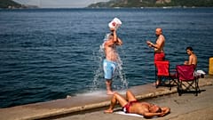 Люди охлаждаются на берегу Босфора на фоне дыма от лесных пожаров в жаркий летний день в Стамбуле, Турция, июль 2023 года. 
