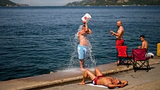 Люди охлаждаются на берегу Босфора на фоне дыма от лесных пожаров в жаркий летний день в Стамбуле, Турция, июль 2023 года. 