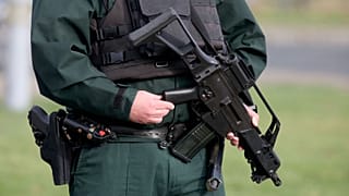 An armed police officer stands guard as the shooting of John Caldwell is investigated in February.