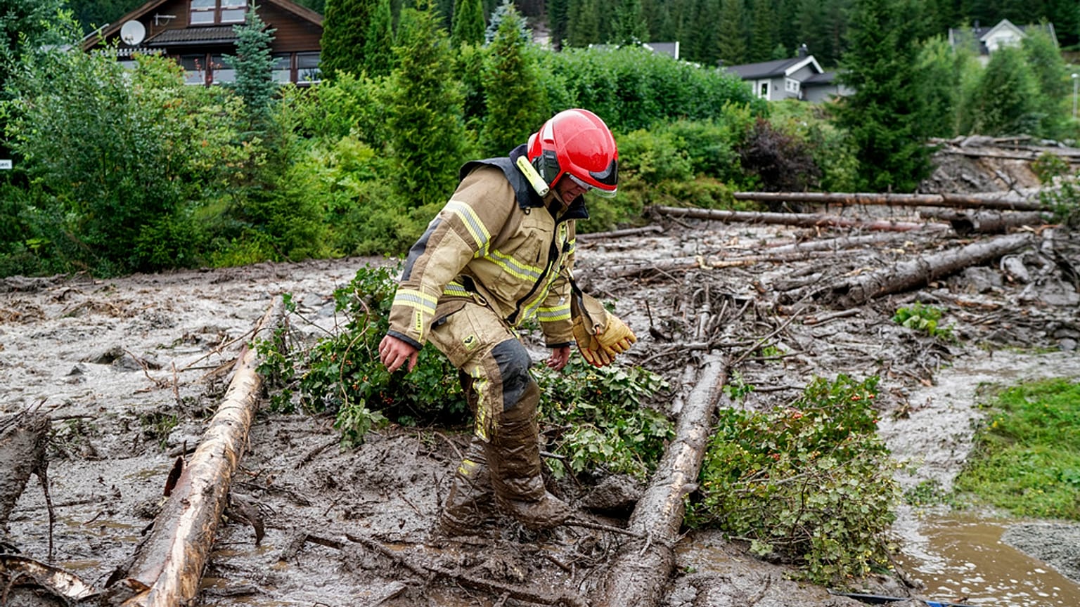 A rescue worker climbs over tree trunks after a mudslide has hit several residential buildings in Bagn in Valdres, Norway, Tuesday, Aug. 8, 2023. 