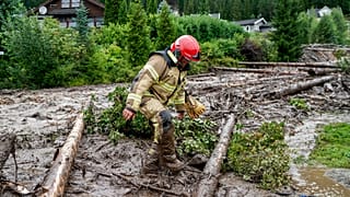 A rescue worker climbs over tree trunks after a mudslide has hit several residential buildings in Bagn in Valdres, Norway, Tuesday, Aug. 8, 2023. 