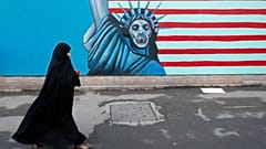 امرأة إيرانية محجبة من الرأس إلى أخمص القدمين تمشي أمام رسم ساخر لتمثال الحرية, رسمت على جدار السفارة الأمريكية السابقة في طهران
