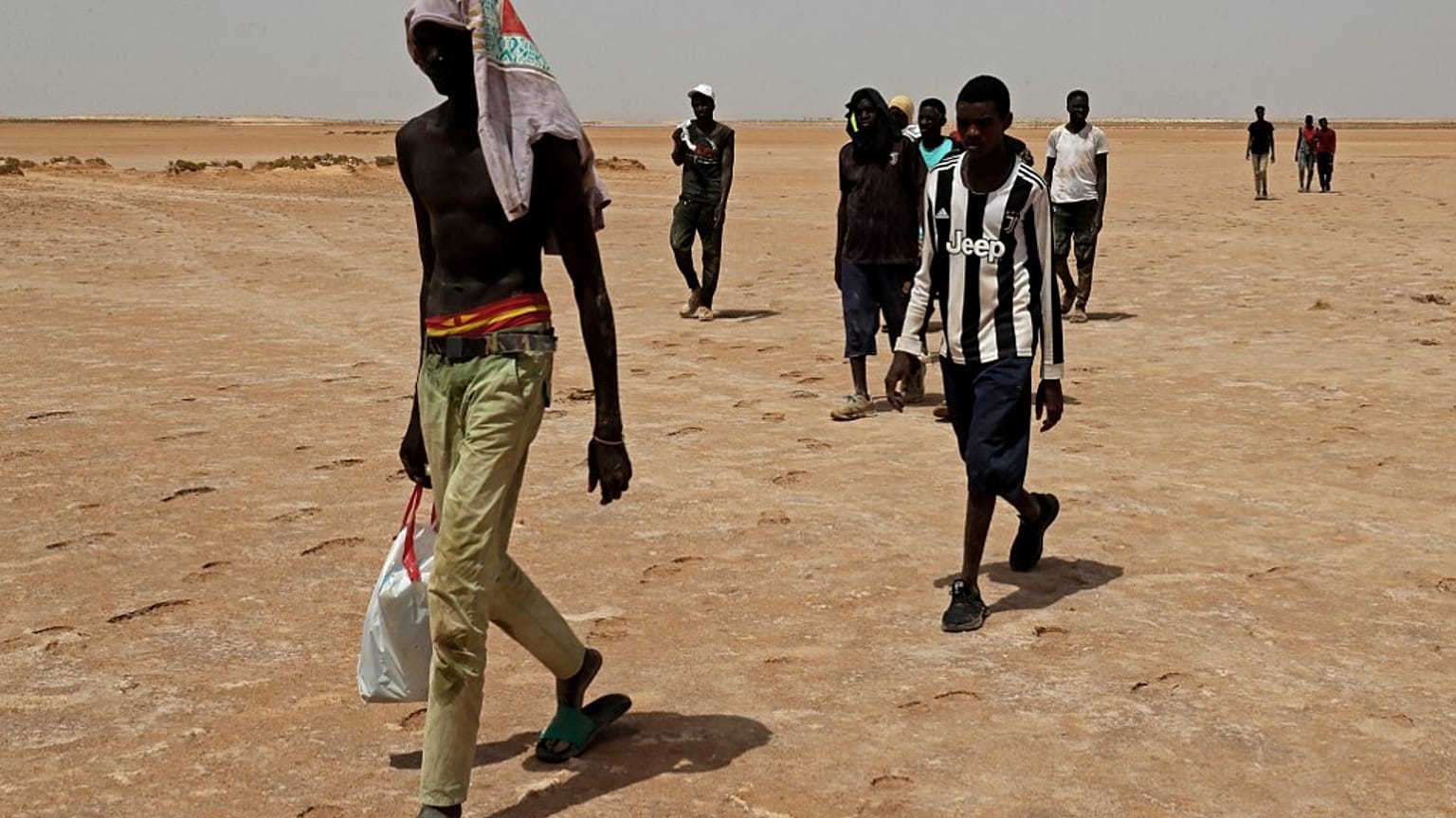 Des migrants d'origine africaine qui auraient été abandonnés par les autorités tunisiennes, marchent dans la chaleur à la frontière libyo-tunisienne, le 30 juillet 2023.