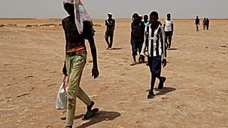 Des migrants d'origine africaine qui auraient été abandonnés par les autorités tunisiennes, marchent dans la chaleur à la frontière libyo-tunisienne, le 30 juillet 2023.