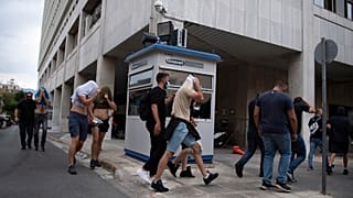 Adeptos de futebol, na sua maioria croatas, cobrem a cara enquanto a polícia os escolta da Direção-Geral da Polícia de Ática para o tribunal, em Atenas, Grécia, no domingo, 13 de agosto,