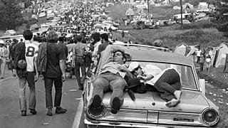 Woodstock attendees catch a nap on top of a car, 1969