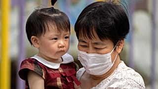 Archivo: una mujer con mascarilla lleva en brazos a un niño mientras pasean por un parque público de Pekín, el 1 de junio de 2023.