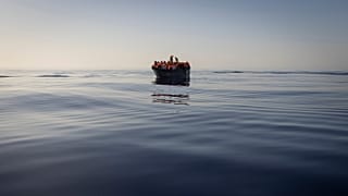People equipped with life jackets set sail in a wooden boat in the Mediterranean Sea.