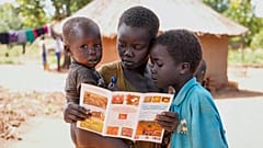 ثلاثة أطفال في السودان يقرؤون كتيبا 