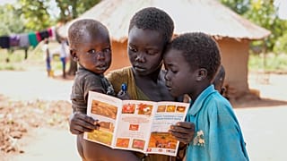 ثلاثة أطفال في السودان يقرؤون كتيبا 