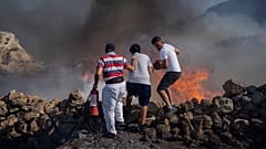 ثلاثة أشخاص يحاولون جهدهم إطفاء حريق في منتجع ليندوس بجزيرة رودس