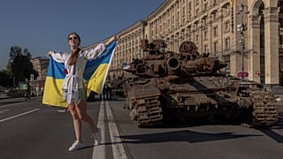 FILE - A woman poses for photos holding the Ukrainian flag next to destroyed Russian armoured military vehicles on display in Kyiv, on August 24, 2023.