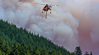A helicopter flies between the Bedrock Fire and nearby Fall Creek to get a load of water as the wildfire burns east of Eugene, Ore.