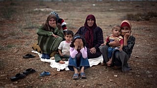 Une famille syrienne qui a fui les violences dans son village est assise par terre dans un camp de déplacés dans le village syrien d'Atmeh, près de la frontière turque avec la Syrie.