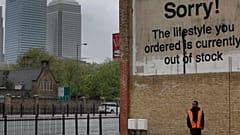 A man walks in east London, backdropped by high rise buildings at the Canary Wharf financial district.
