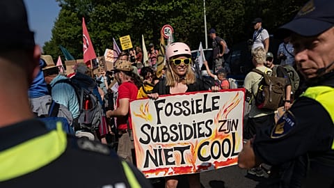 A protestor holds a sign reading "Fossil Subsidies Are Not Cool" as she blocks a highway near the Dutch parliament in The Hague, Netherlands, Sept. 9, 2023. 