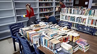 أشخاص ينظفون رفوف كتب في مكتبة مدرسة في اللويزة قرب بيروت