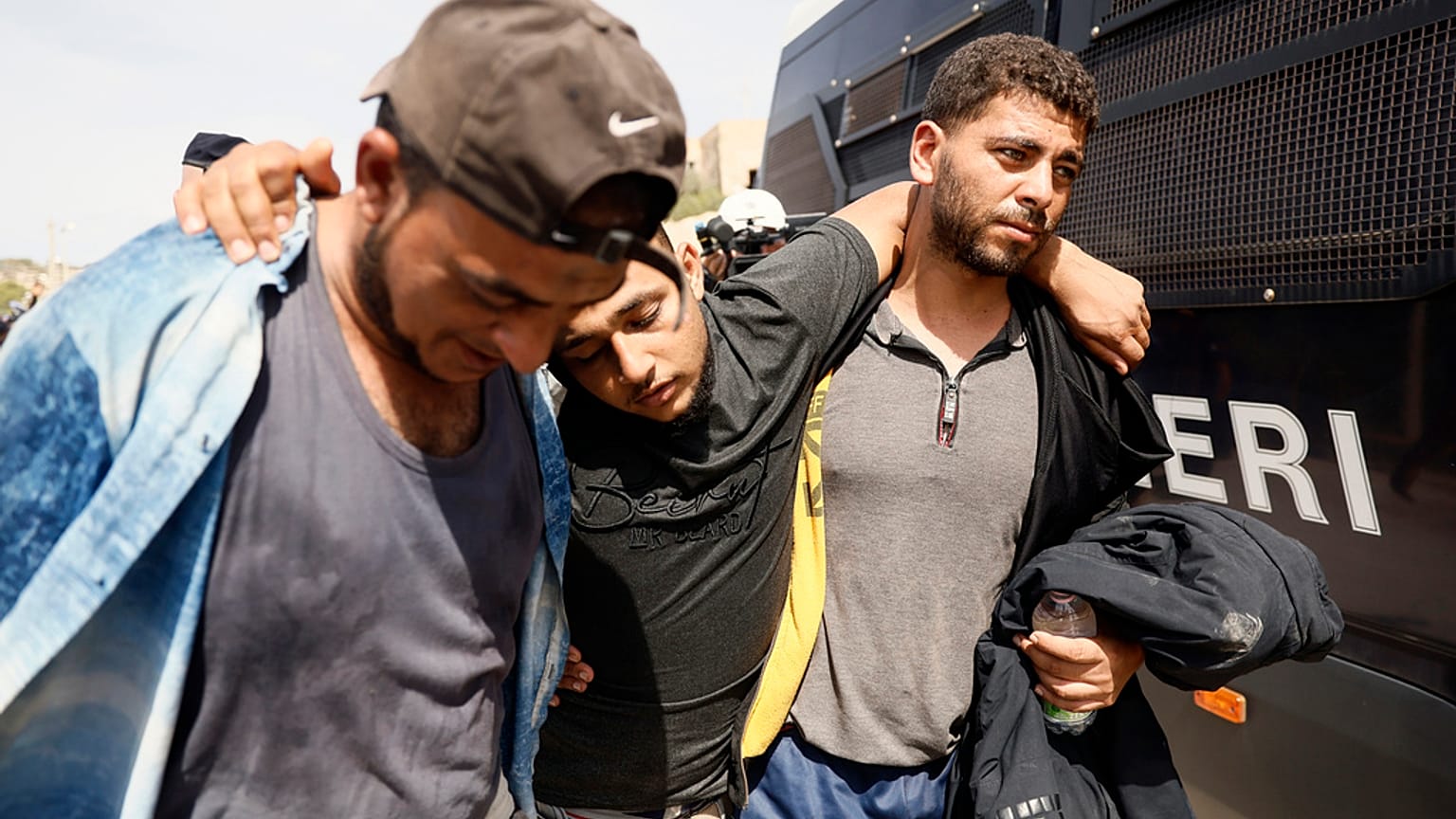 Migrantes entreajudam-se enquanto deixam o centro de receção sobrelotado, em Lampedusa, Itália