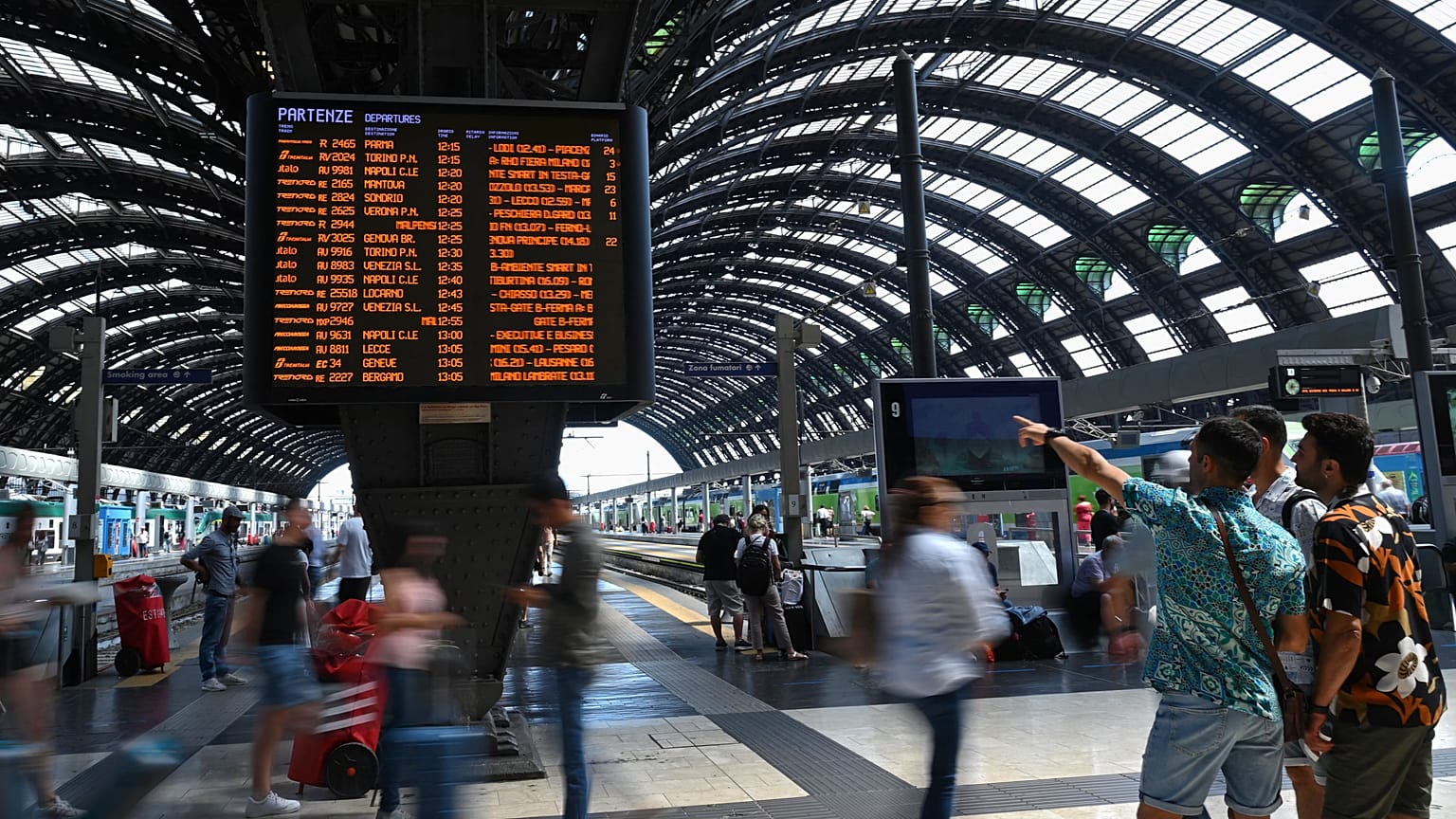 Viaggiatori controllano sui tabelloni ferroviari le variazioni degli orari alla stazione centrale di Milano  
