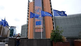 Flags flap in the wind as a man with flowers walks by EU headquarters in Brussels, Wednesday, Sept. 20, 2023.