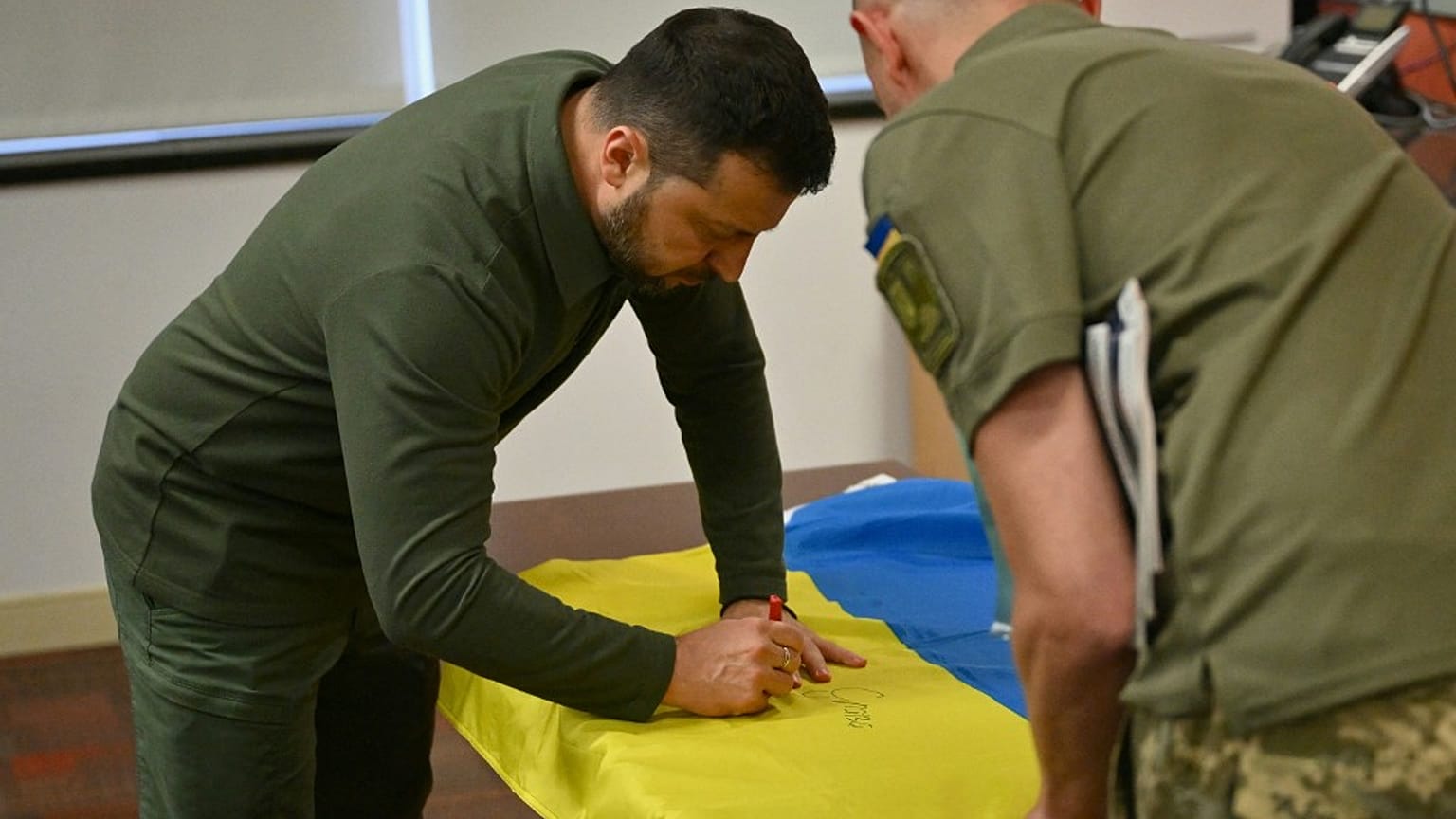 Il presidente ucraino Volodymir Zelensky autografa la bandiera nazionale per un soldato
