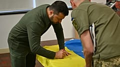 Il presidente ucraino Volodymir Zelensky autografa la bandiera nazionale per un soldato