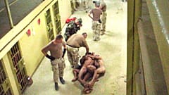  صورة حصلت عليها صحيفة واشنطن بوست ونشرت يوم  6 مايو/أيار 2004، تظهر عسكريين أمريكيين مع معتقلين عراة مقيدين ببعضهم البعض على الممشى أمام السجناء الآخرين في سجن أبو غريب في بغ