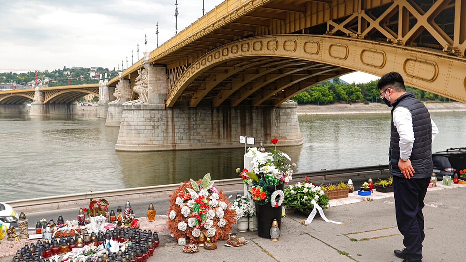 Un hombre junto a velas y flores colocadas sobre el río Danubio durante una ceremonia en memoria de las víctimas, un año después del accidente del barco.