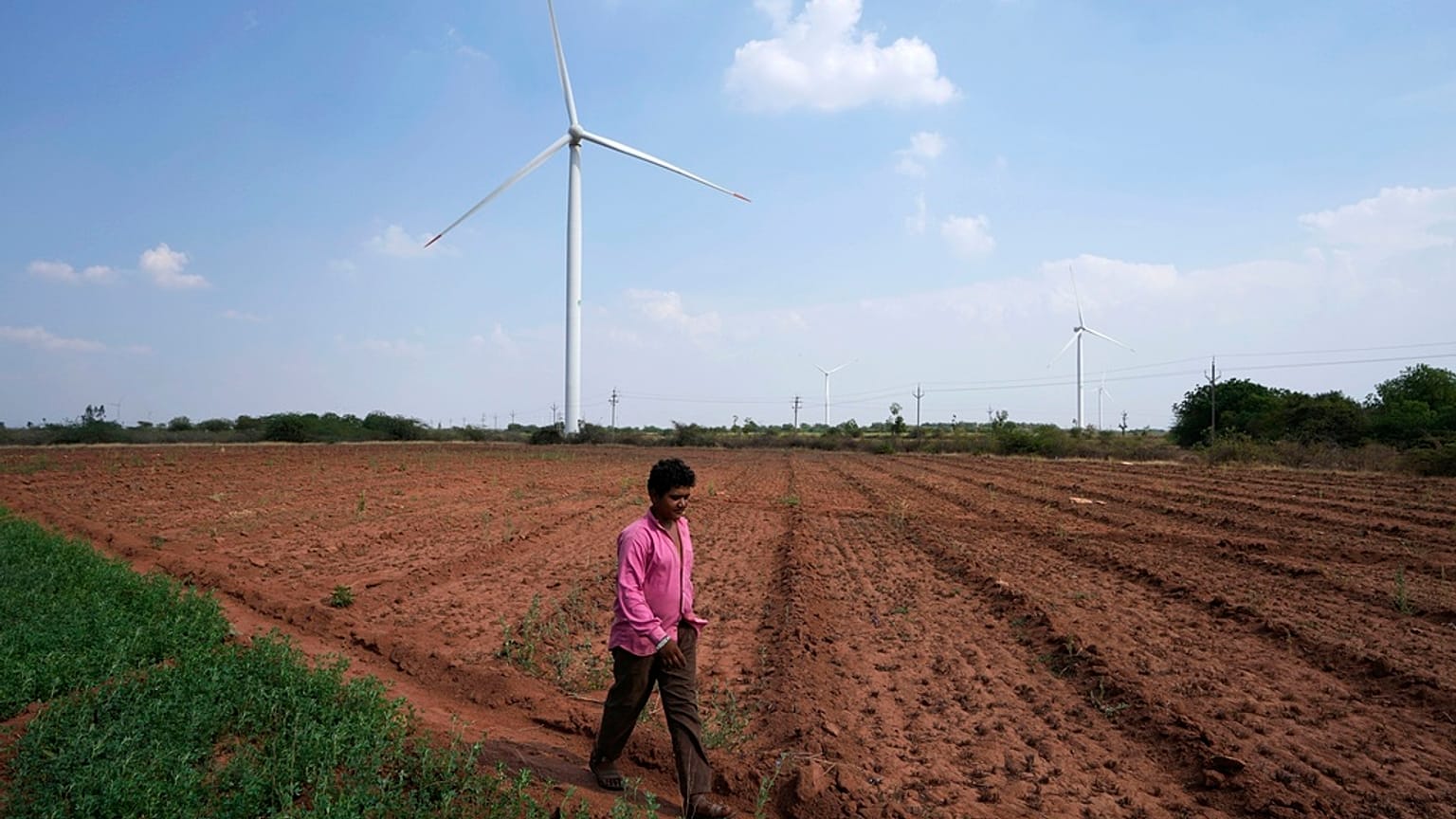 File - A boy walks on a field near wind turbines near Sadla village in Surendranagar district of Gujarat state, India, March 20, 2023.