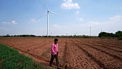 File - A boy walks on a field near wind turbines near Sadla village in Surendranagar district of Gujarat state, India, March 20, 2023.