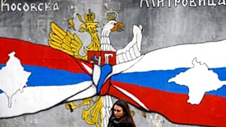FILE - A woman walks by graffiti showing the Serbian flag, left, and Russian flags with maps of Kosovo and Crimea in northern Kosovo, 15/12/2018.