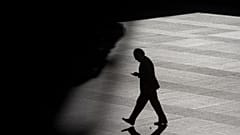 A man looks as his cell phone as he walks into the shadows in the business district in Madrid, Spain.